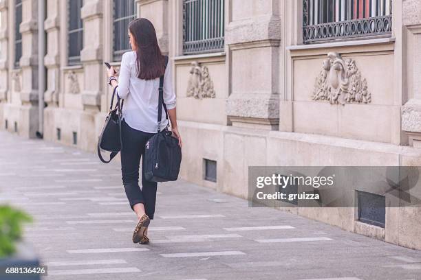 jonge zakenvrouw met behulp van mobiele telefoon op haar weg naar werk - brunette woman back stockfoto's en -beelden