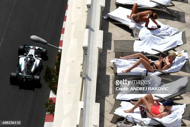 Women sunbath as Mercedes' British driver Lewis Hamilton steers his car during the second practice session at the Monaco street circuit on May 25,...