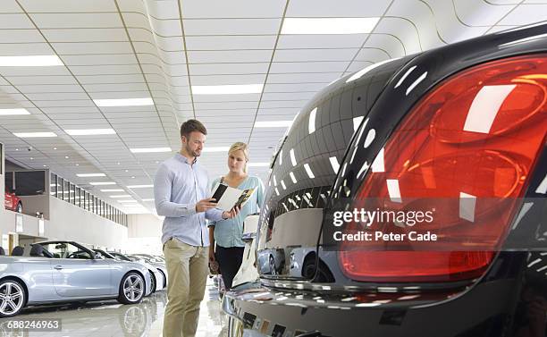 couple looking at brochure in car showroom - auto dealership stock pictures, royalty-free photos & images
