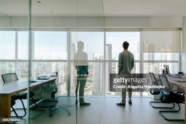 young man looks out of office window over city - dorsale foto e immagini stock