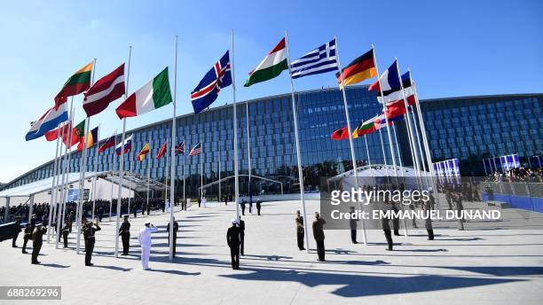 Officials and military personnel stand beneath flags as they attend the NATO summit ceremony at the NATO headquarters, in Brussels, on May 25, 2017.