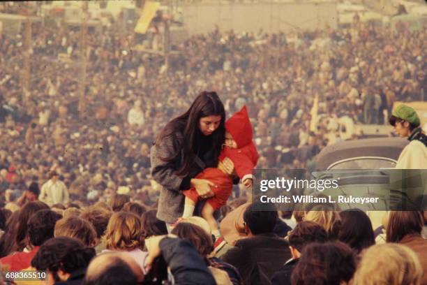 Woman carries a child through the massive audience at the Altamont Speedway prior to the free concert headlined by the Rolling Stones.