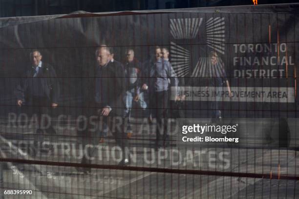 Pedestrians crossing the street are seen through a road closure sign in Toronto, Ontario, Canada, on Friday, May 19, 2017. Ontario is easing rules...