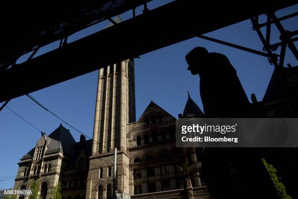 The silhouette of a pedestrian is seen passing in front of old City Hall in Toronto, Ontario, Canada, on Friday, May 19, 2017. Ontario is easing...