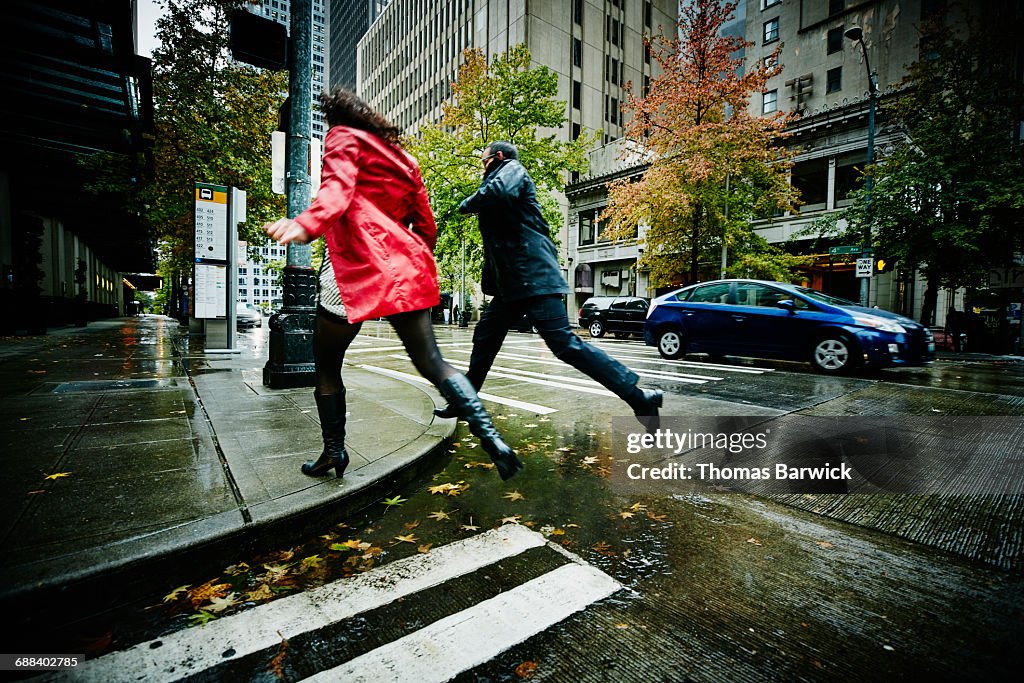 Couple jumping over puddle on city street