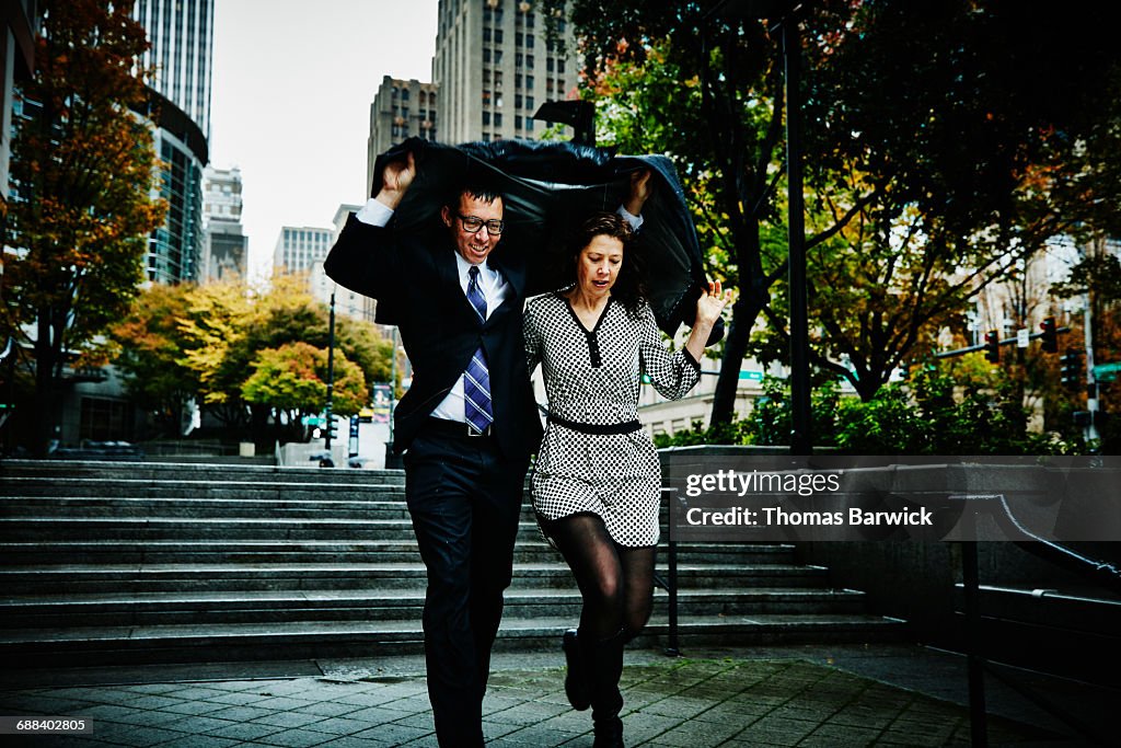 Couple running down stairs holding coat over heads