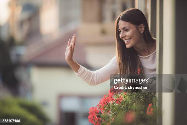 beautiful woman greeting someone on the street from her house window. - balcony window stock pictures, royalty-free photos & images