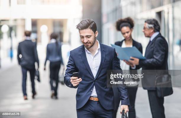 business people walking outside the business building - man looking at phone in public stock pictures, royalty-free photos & images