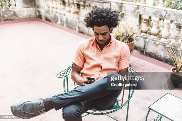 handsome afro-caribbean cuban man in chair looking on mobile