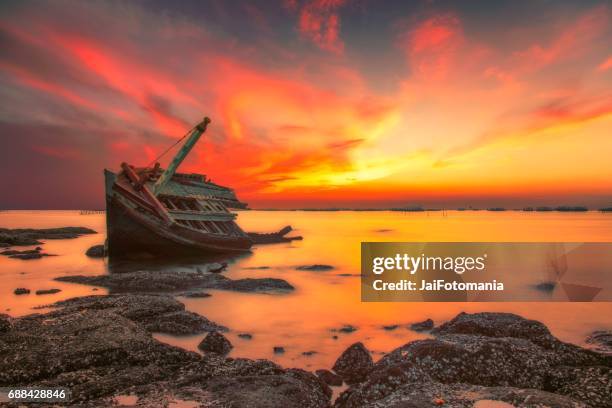 an old shipwreck or abandoned shipwreck.,boat capsized on a rocky beach in beautiful sunset background - buque 個照片及圖片檔