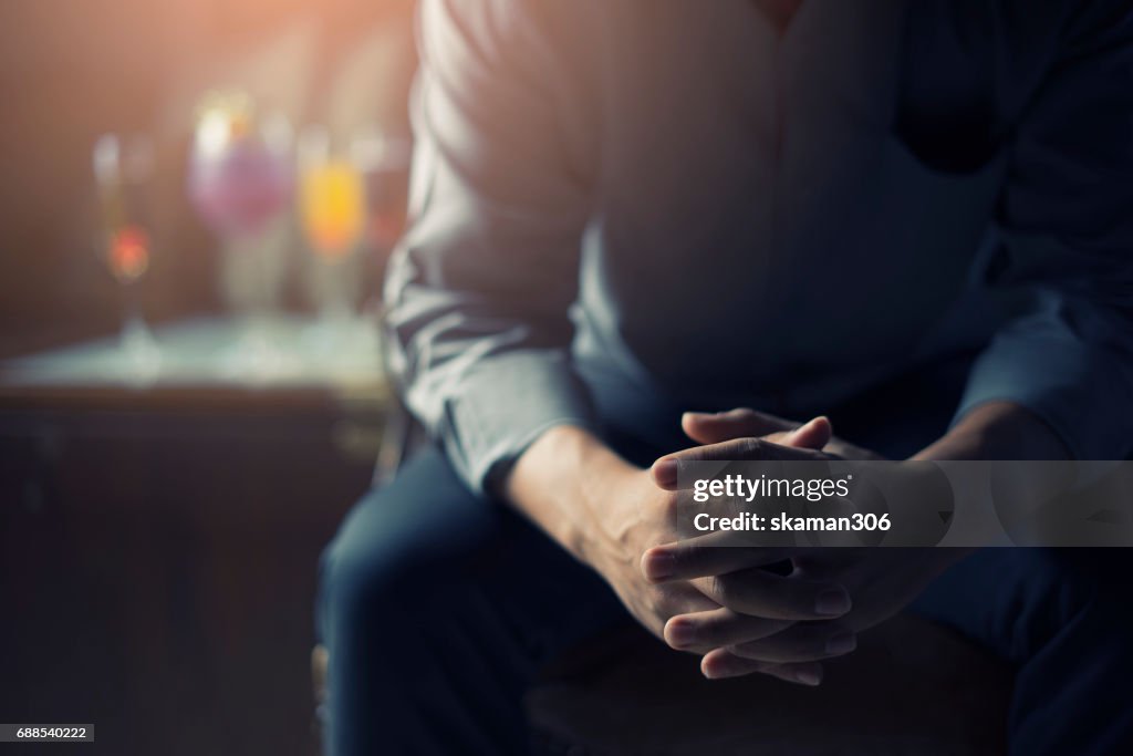 Very Tired or stressed businessman hand touching head and sitting in front of cocktail and alcohol drink with darken mood and tone