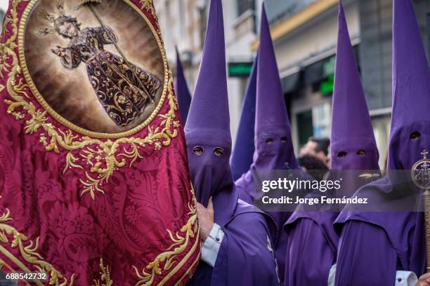 Nazarenos participating in a religious procession, with the traditional robes and hoods and carrying a banner for their brotherhood during Semana...