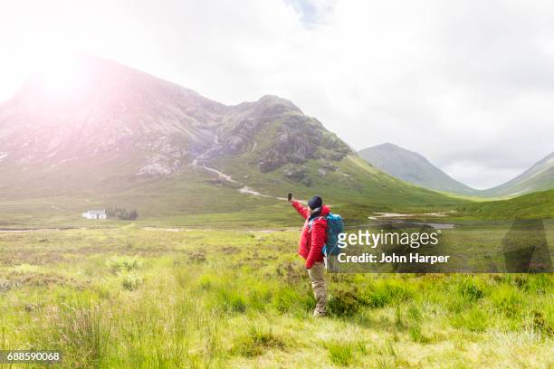 man using mobile phone to take photo of scenery in scottish highlands. - hiking rucksack stock pictures, royalty-free photos & images