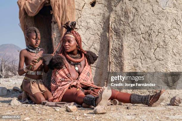 Himba girl combing the hair of one of her relatives. Himbas are a bantu tribe who migrated into what today is Namibia a few centuries ago. They...