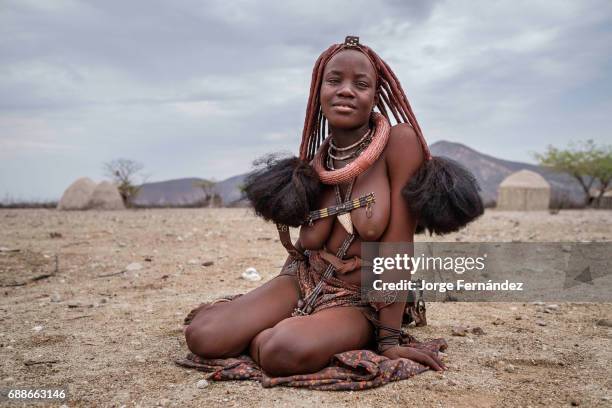 Portrait of a Himba woman sitting on the ground in a small village. Himbas are a bantu tribe who migrated into what today is Namibia a few centuries...