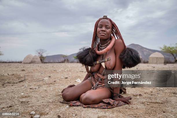 Portrait of a Himba woman sitting on the ground in a small village. Himbas are a bantu tribe who migrated into what today is Namibia a few centuries...