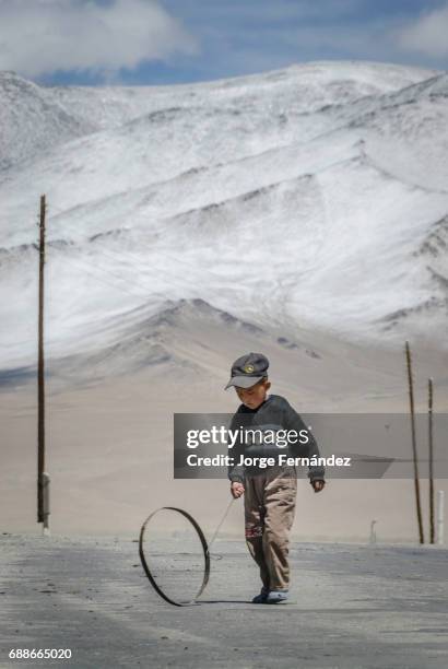 Boy playing with a wheel in a lone road in the desert with mountains in the background.