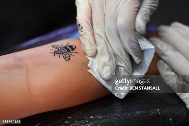 Tattoo artist inks a bee logo, synonymous with Manchester as a symbol of the city's industrial heritage, and rapidly becoming a symbol of resilience...