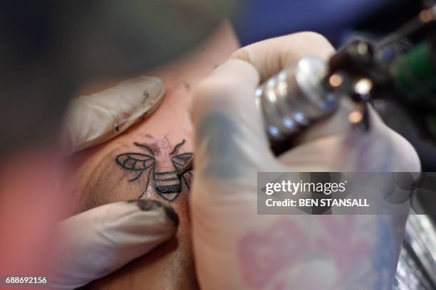 Tattoo artist inks a bee logo, synonymous with Manchester as a symbol of the city's industrial heritage, and rapidly becoming a symbol of resilience...