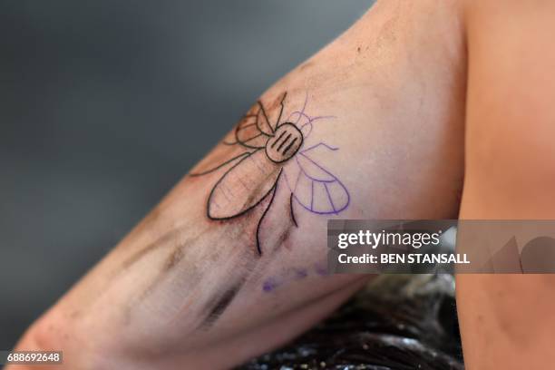 Tattoo artist inks a bee logo, synonymous with Manchester as a symbol of the city's industrial heritage, and rapidly becoming a symbol of resilience...