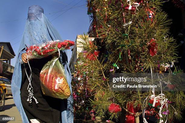 An Afghanistan woman in a burka walks by a Christmas tree on display December 23, 2001 on Flower Street in downtown Kabul, Afghanistan. Some...