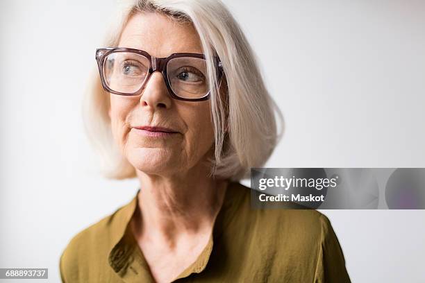 thoughtful senior woman wearing eyeglasses against white background - mirada de reojo fotografías e imágenes de stock