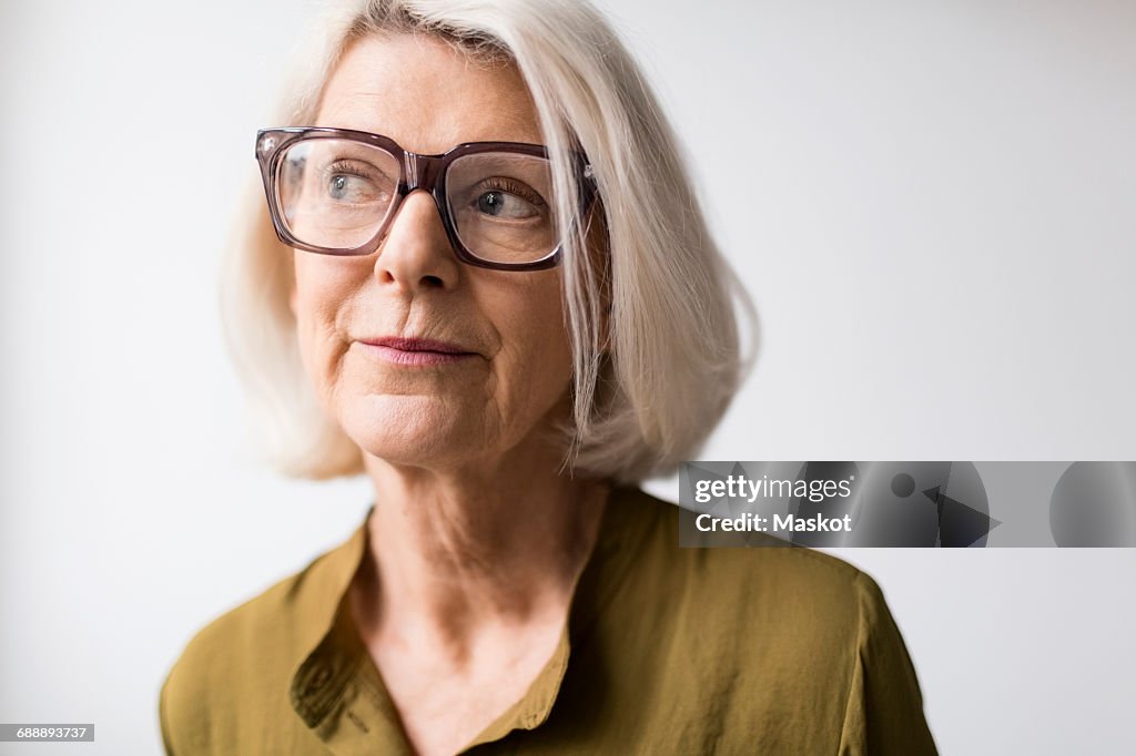 Thoughtful senior woman wearing eyeglasses against white background