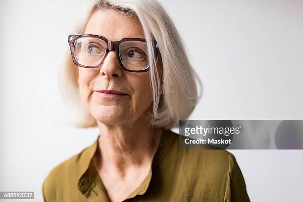thoughtful senior woman wearing eyeglasses against white background - sideways glance - fotografias e filmes do acervo