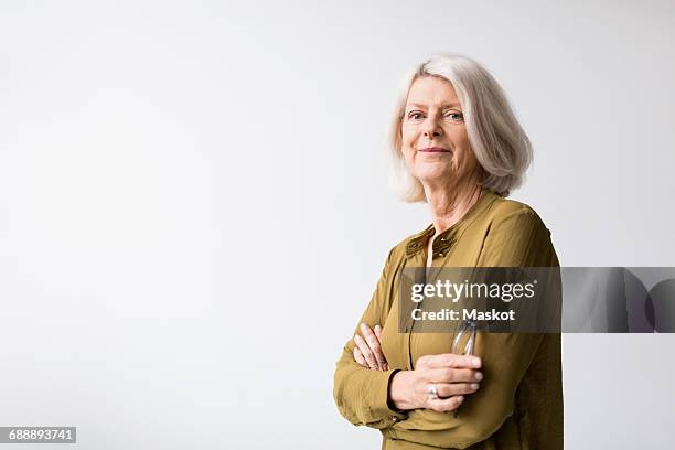 portrait of confident senior woman standing arms crossed against white background - portrait woman white background stock-fotos und bilder