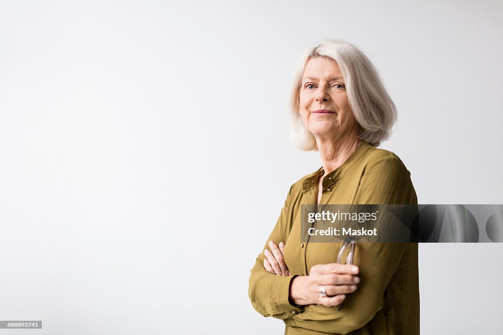 Portrait of confident senior woman standing arms crossed against white background