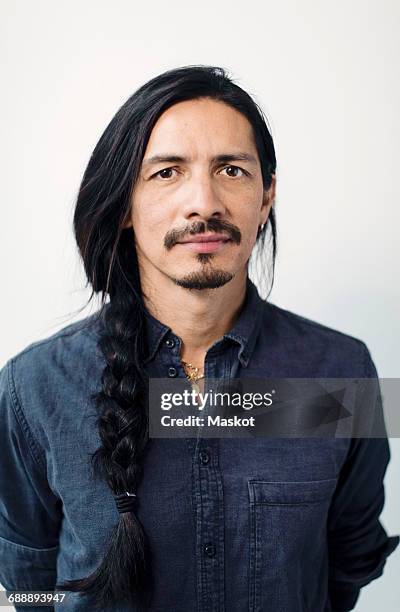 Portrait of confident mature man with braided hair standing against white background