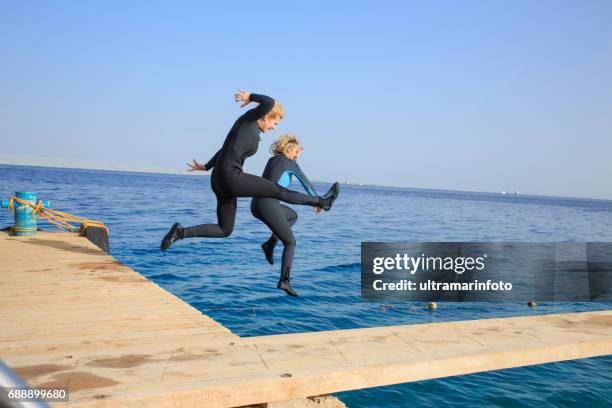 summer fun water sports team. pretty scuba diver, two attractive, vital, mature women. jumping in sea. dressed in a wet suit. long blonde hair, beautiful blue eyes. sporting women. beautiful blue sea in the background. - marina stock pictures, royalty-free photos & images