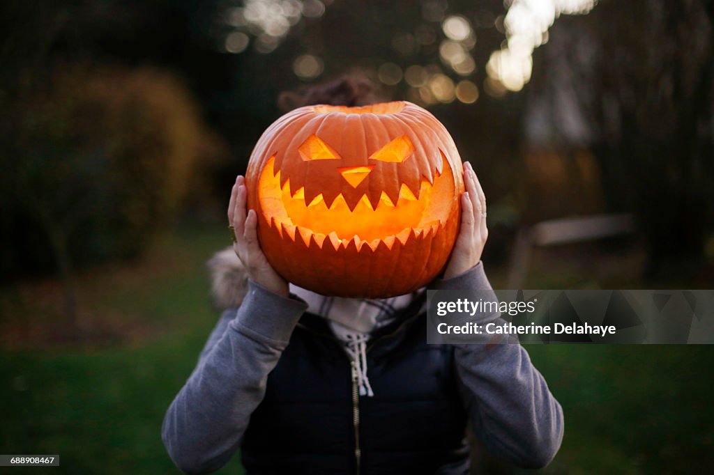 A girl with Halloween pumpkin in front of her head