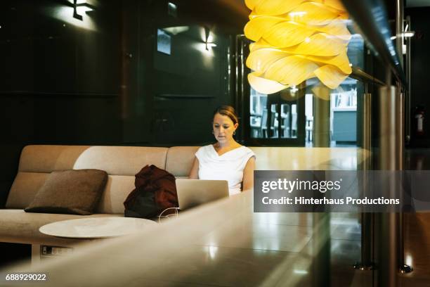 businesswoman sitting working on laptop in hotel bar - businesswoman hotel stock pictures, royalty-free photos & images