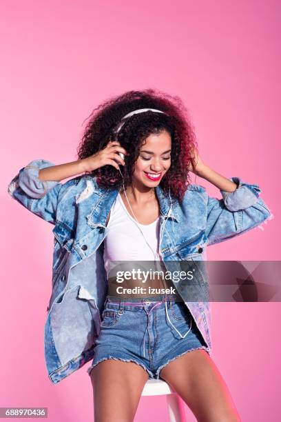 junge afro frau anhören von musik - rosa shorts stock-fotos und bilder
