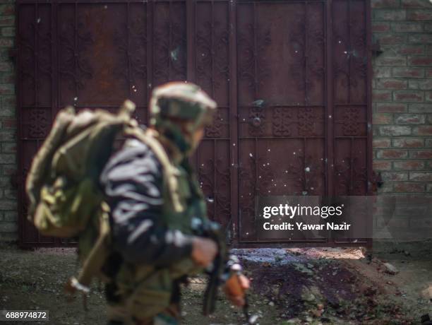 An Indian army trooper walks past a bullet-riddled door and blood stained ground where top rebel commander of Hizbul Mujahideen Sabzar Ahmed , along...