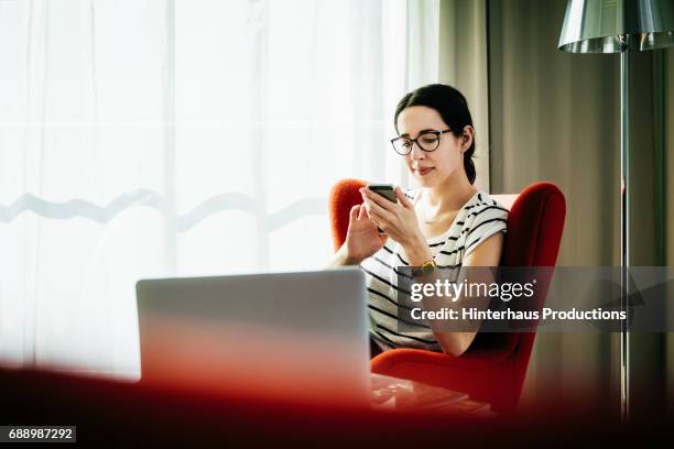 young woman sitting down using smartphone in hotel room - character stock photos et images de collection