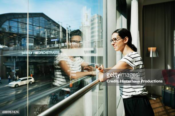 young woman looking out hotel room window - car reflection stock-fotos und bilder