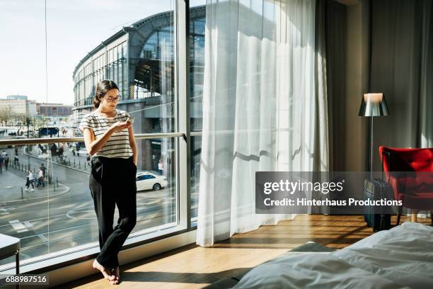 young woman stood using phone in modern hotel room - leaning ストックフォトと画像