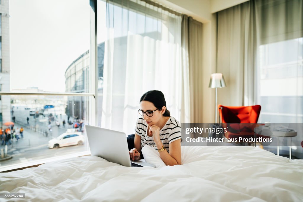 Woman Using Laptop On A Bed In Hotel Room