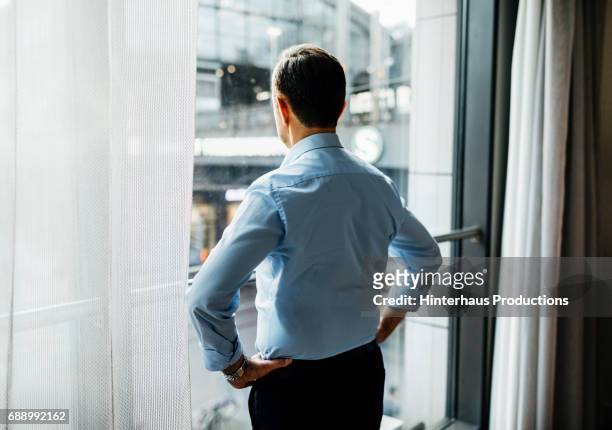 businessman taking in the view from his hotel room - rückansicht stock-fotos und bilder