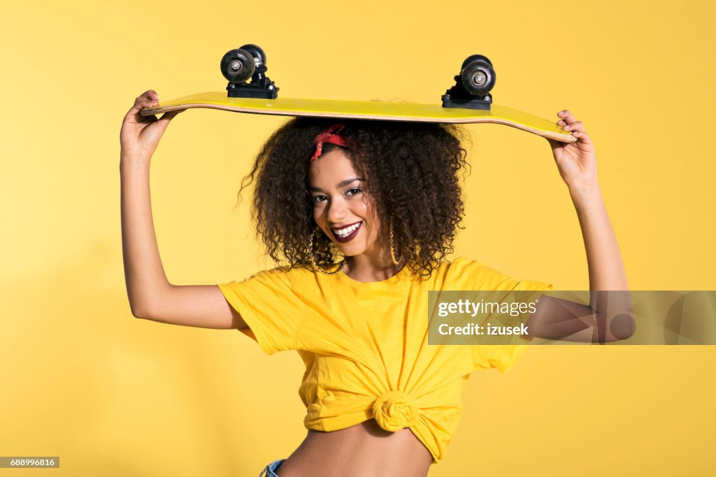 Happy young afro woman holding skateboard on her head