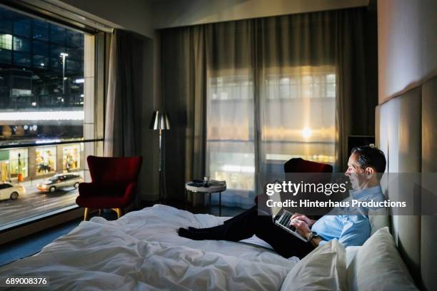businessman sat on hotel bed working - sitting on a bed stock pictures, royalty-free photos & images