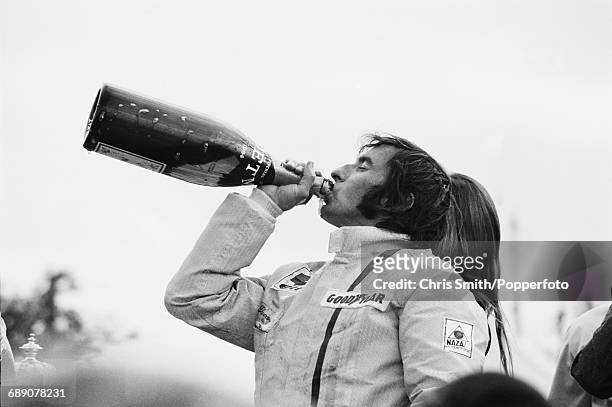 British Formula One racing driver Jackie Stewart drinks from an oversized bottle of Moet & Chandon champagne after driving the Elf Team Tyrrell 003...