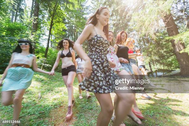 giovani donne che corrono giù per la collina verde verso il lago in estate - running shorts foto e immagini stock