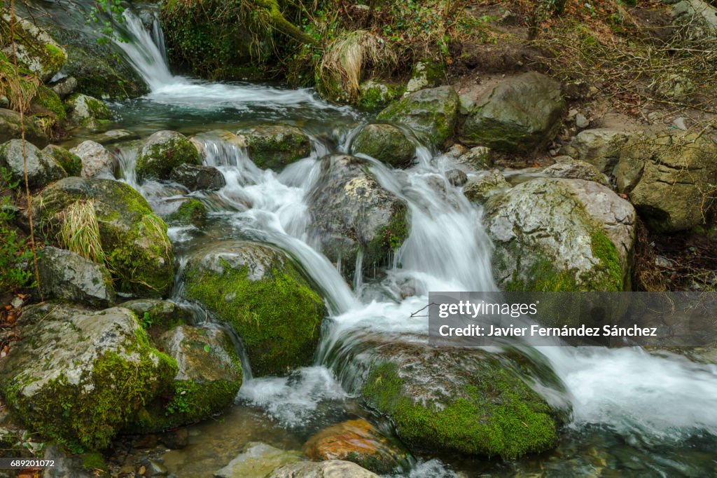 A mountain stream of crystalline water flows between rocks with small waterfalls.