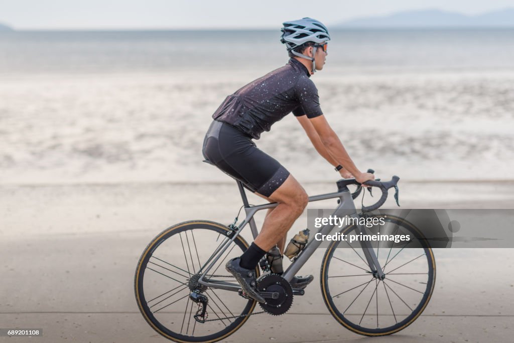 Homem jovem asiático ciclista andar de bicicleta na praia por do sol