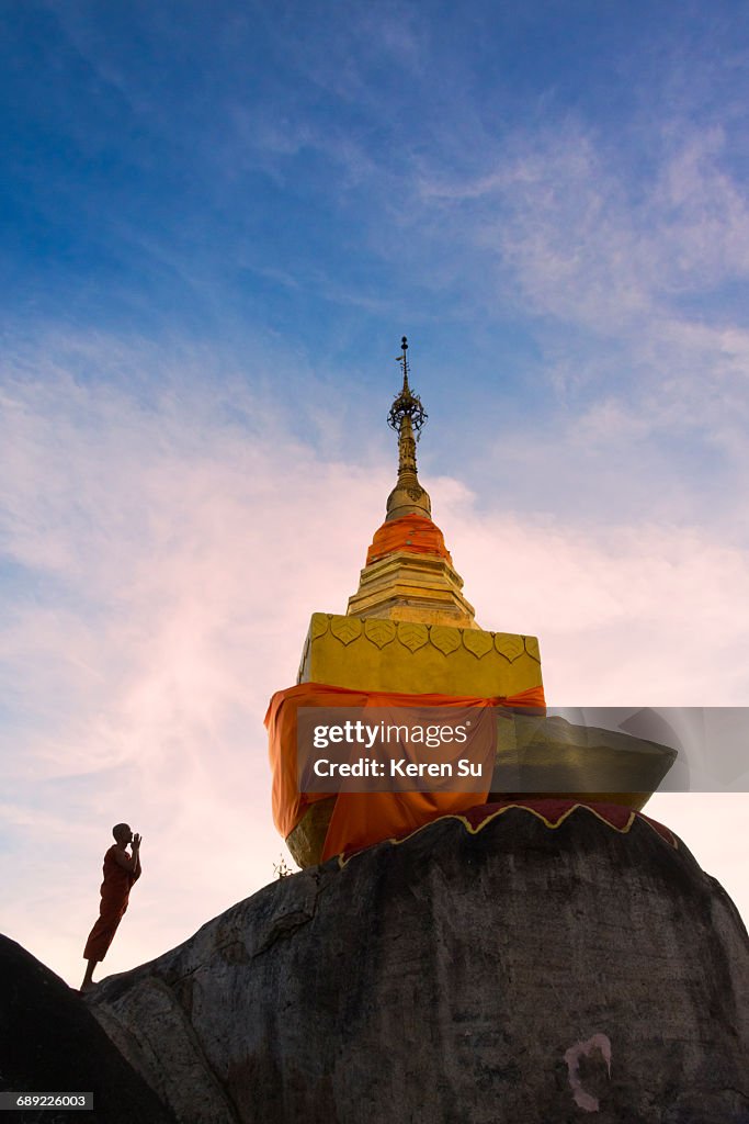 Monk praying at a golden pagoda on Mt Kyaiktiyo