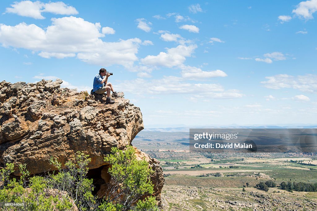 Photographer sitting on hill taking a photograph.