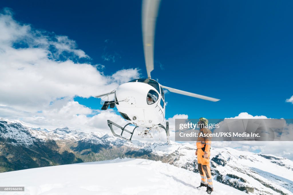 Helicopter lands on mountain summit, ground crew member guides below